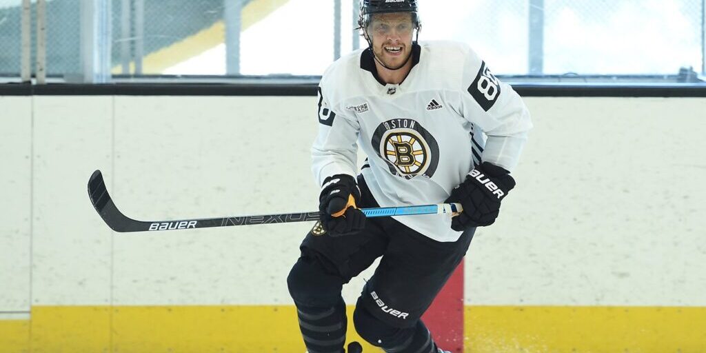 A Boston Bruins player in a white practice jersey skating on the ice during a drill
