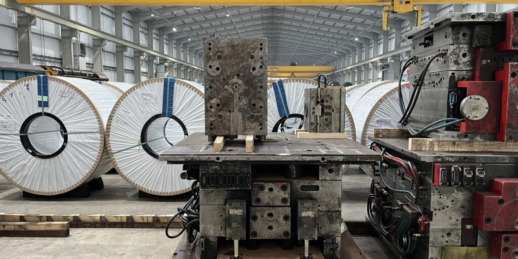 Large metal coils and industrial machinery inside a steel manufacturing warehouse