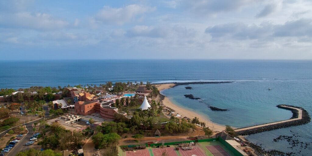 Aerial view of a Dakar coastal resort with outdoor sports courts, a pool and a sea breakwater.
