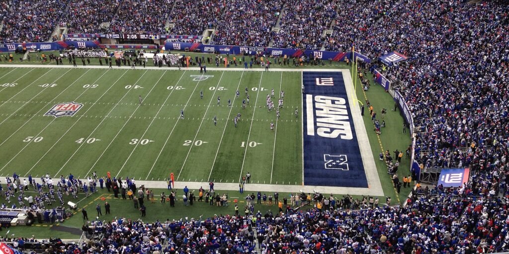 Packed crowd watches New York Giants players on the field at MetLife Stadium during a game.