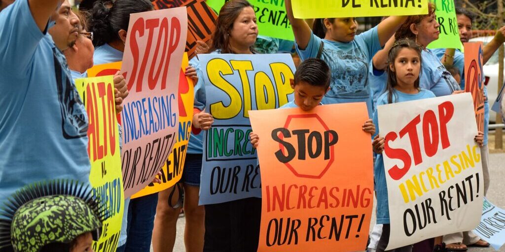 Protesters holding signs calling to stop rent increases at a NYC Rent Guidelines Board hearing