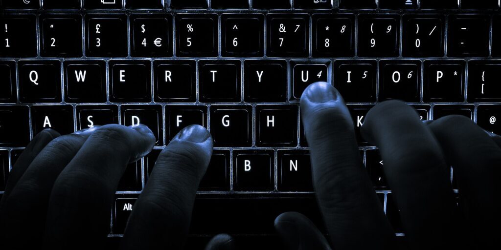 Hands typing on a backlit laptop keyboard in the dark, with one finger pressing the U key
