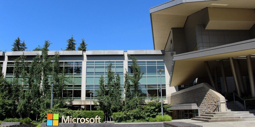 Modern glass and stone office building with a Microsoft logo sign in front, under a clear blue sky.