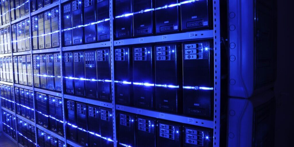 Rows of dark server units on metal shelves, lit by blue light strips in a server room