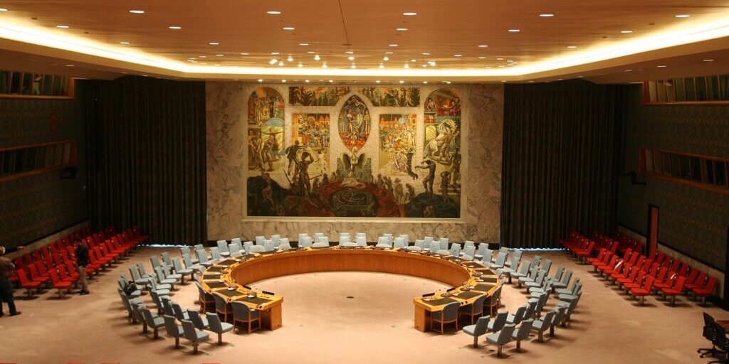 Empty UN Security Council chamber with blue and red delegates' seats arranged in a circle