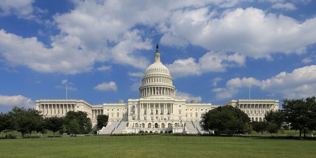 U.S. Capitol building photographed from a distance with green lawn and blue sky