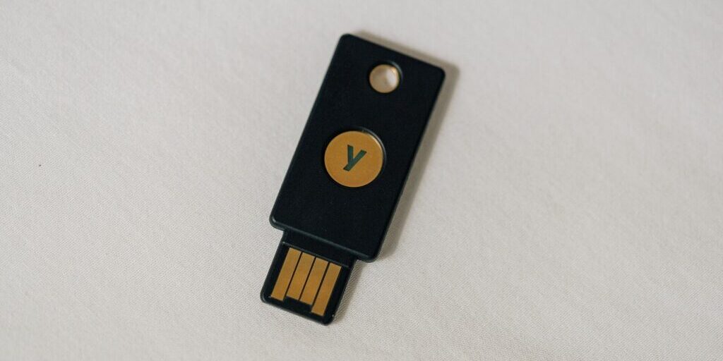 Black YubiKey security key with a gold touch button and USB-A connector, lying on a light fabric surface.
