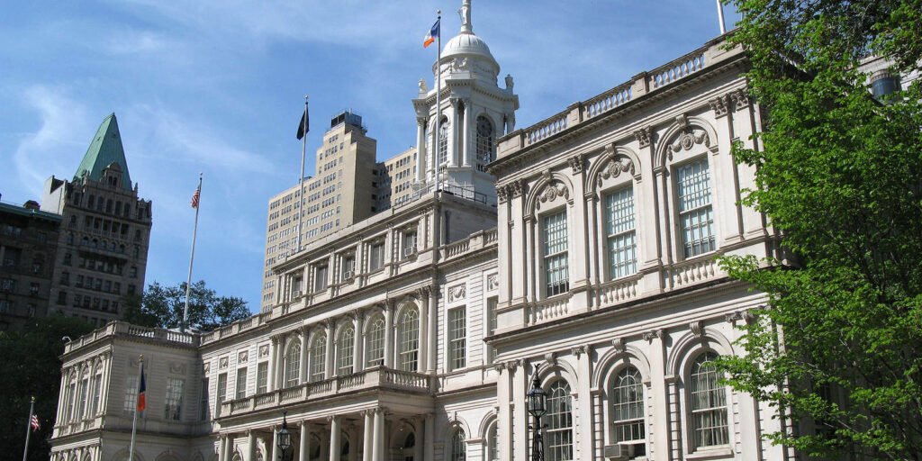 New York City Hall, a white stone building with columns and a domed clock tower, under a blue sky
