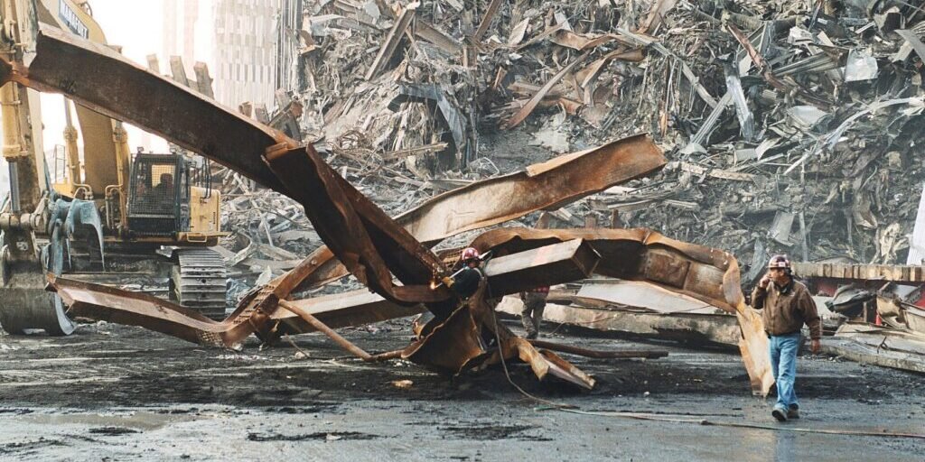 Twisted steel beams and rubble at the World Trade Center site with a worker walking past heavy machinery